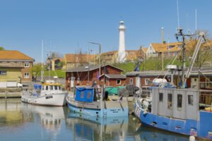 Fischkutter im Hafen, dahinter der weiße Leuchtturm von Rønne auf Bornholm