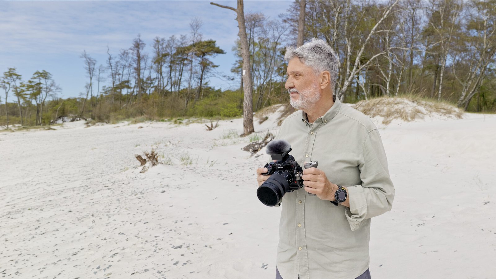 Werner Wilmes mit einer Lumix S1II in der Hand an einem weißen Traumstrand auf der Insel Bornholm. Werner schaut aufs Meer.