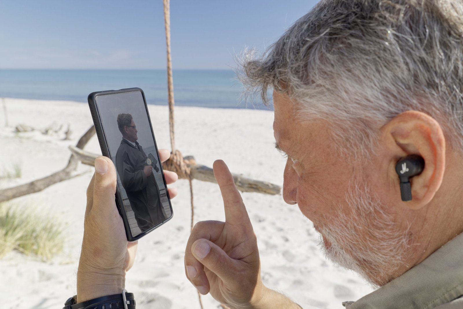 Mann sitzt am Strand und schaut auf sein Smartphone mit dem Bild seines Vaters. Der Mann ist Werner Wilmes